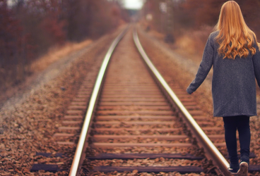 Frau mit langen Haaren balanciert auf einer Eisenbahnschiene